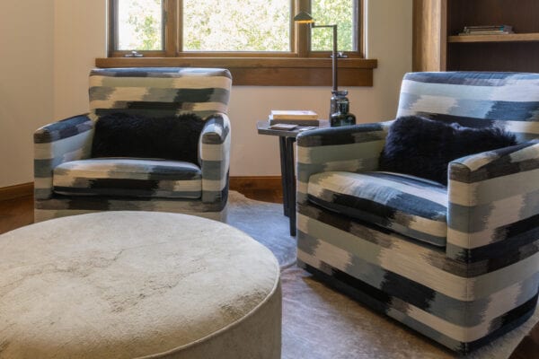 Two matching upholstered chairs, pillows, ottoman, and end table topped with books and knick knacks.
