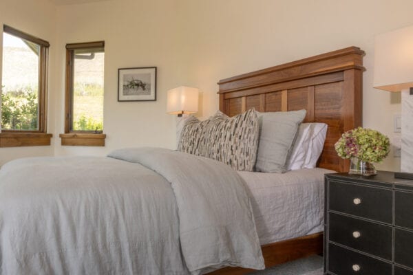A wood framed bed with side table. Atop the table is a bouquet of flowers in a small glass vase and a lamp.