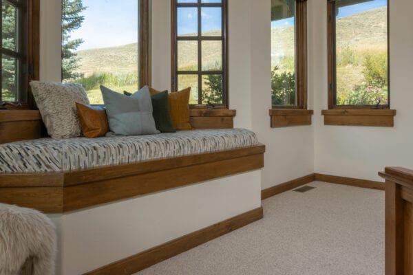 Resting nook with windows behind and various pillows on the cushioned seating area.