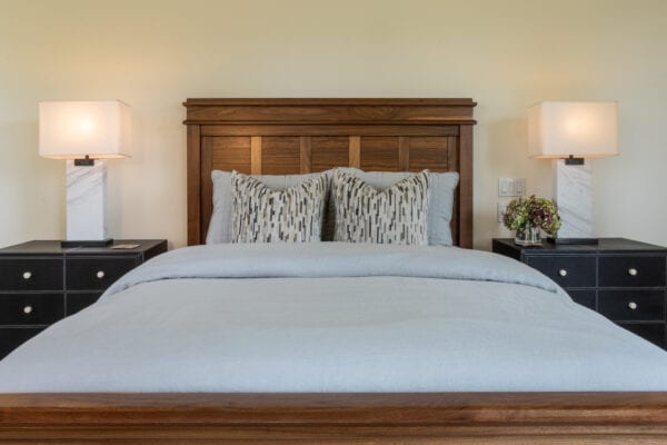 A wood framed bed with matching end tables and lamps on each side.